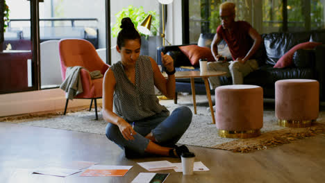 vista frontal de jóvenes colegas de negocios de raza mixta planeando y sentados en el piso de oficinas modernas