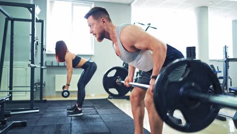 bearded athlete and healthy woman lifting heavy barbells in sport center. concentrated male and a female are doing the same exercise with barbell together in the gym.