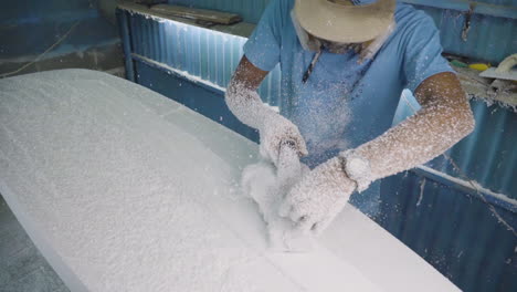 hombre en el taller afeitando la espuma de una tabla de surf de bricolaje con una herramienta de avión manual