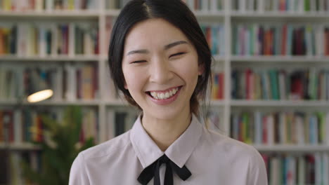 close up portrait of beautiful cute asian woman standing in library laughing and smiling bookcase in background