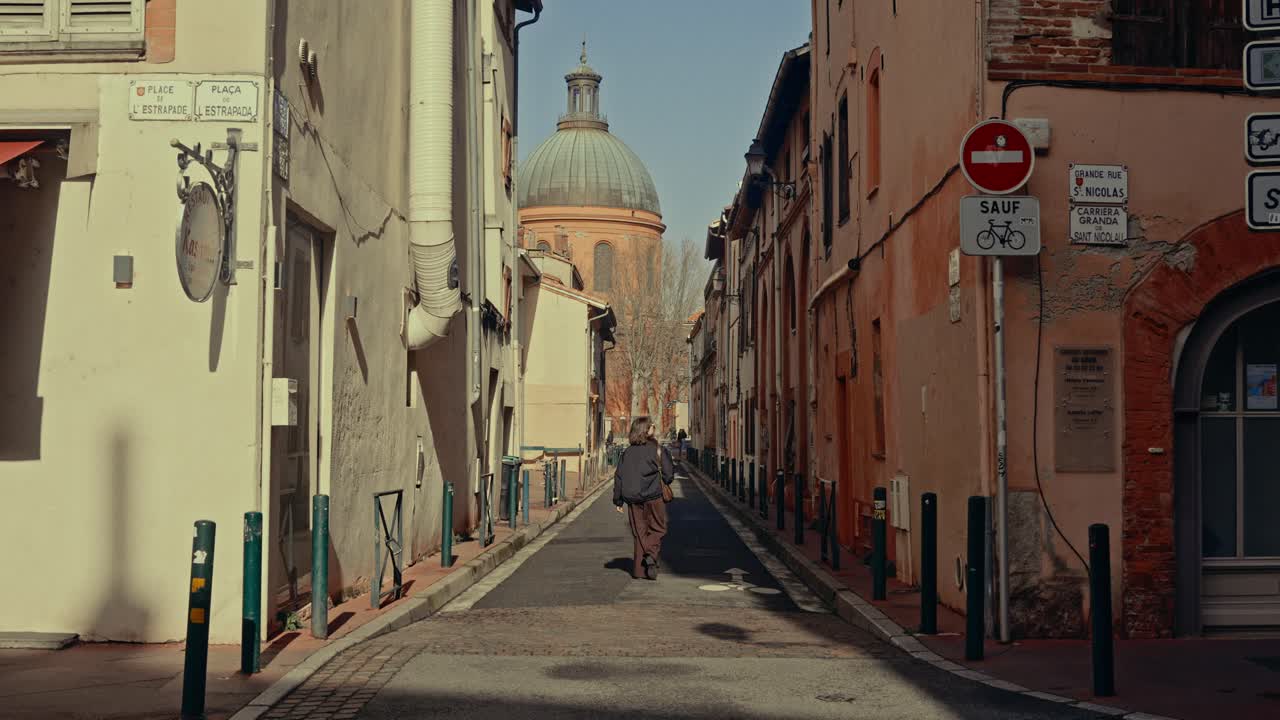 Persona che cammina lungo una stretta via storica di una città europea verso una cupola