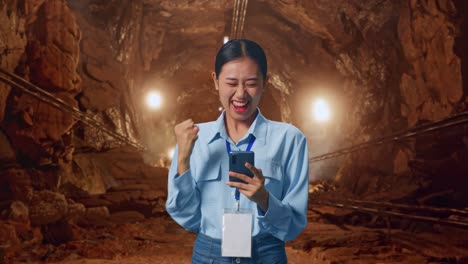 Asian Female With Her Smarphone In Underground Mine Tunnel, She Raises Her Fist Up With Screaming Goal