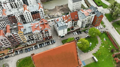 Vista-Aérea-Diagonal-De-Una-Densa-Zona-Urbana-En-Elbląg-Con-Una-Mezcla-De-Edificios-Coloridos,-Coches-Estacionados-Y-Una-Zona-Verde.