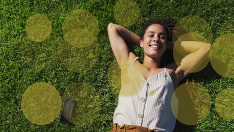 animation of yellow spots over smiling biracial woman lying in park