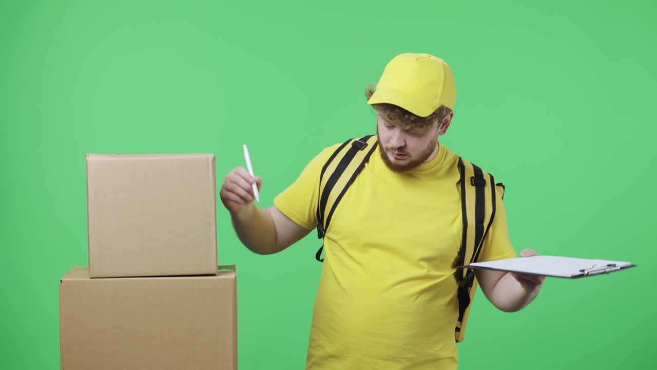 retrato de hombres jóvenes comprobando el número de paquetes y contentos con el resultado. hombre pelirrojo en uniforme de mensajero de entrega amarillo con bolsa térmica posando en pantalla verde. primer plano. cámara lenta lista 59,97 fps