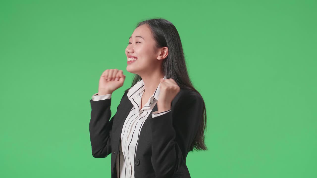 Side View Of A Smiling Asian Business Woman Dancing While Standing On Green Screen Background In The Studio