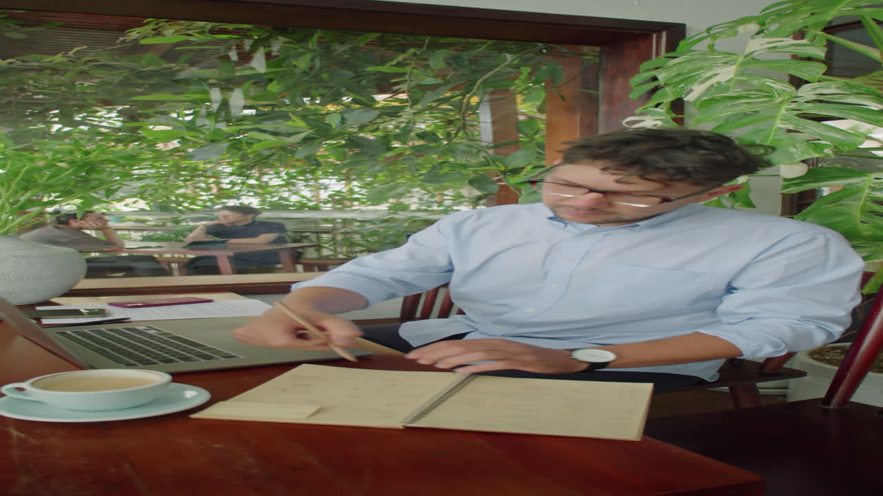 Businessman Using Laptop and Writing in Copybook in Outdoor Cafe