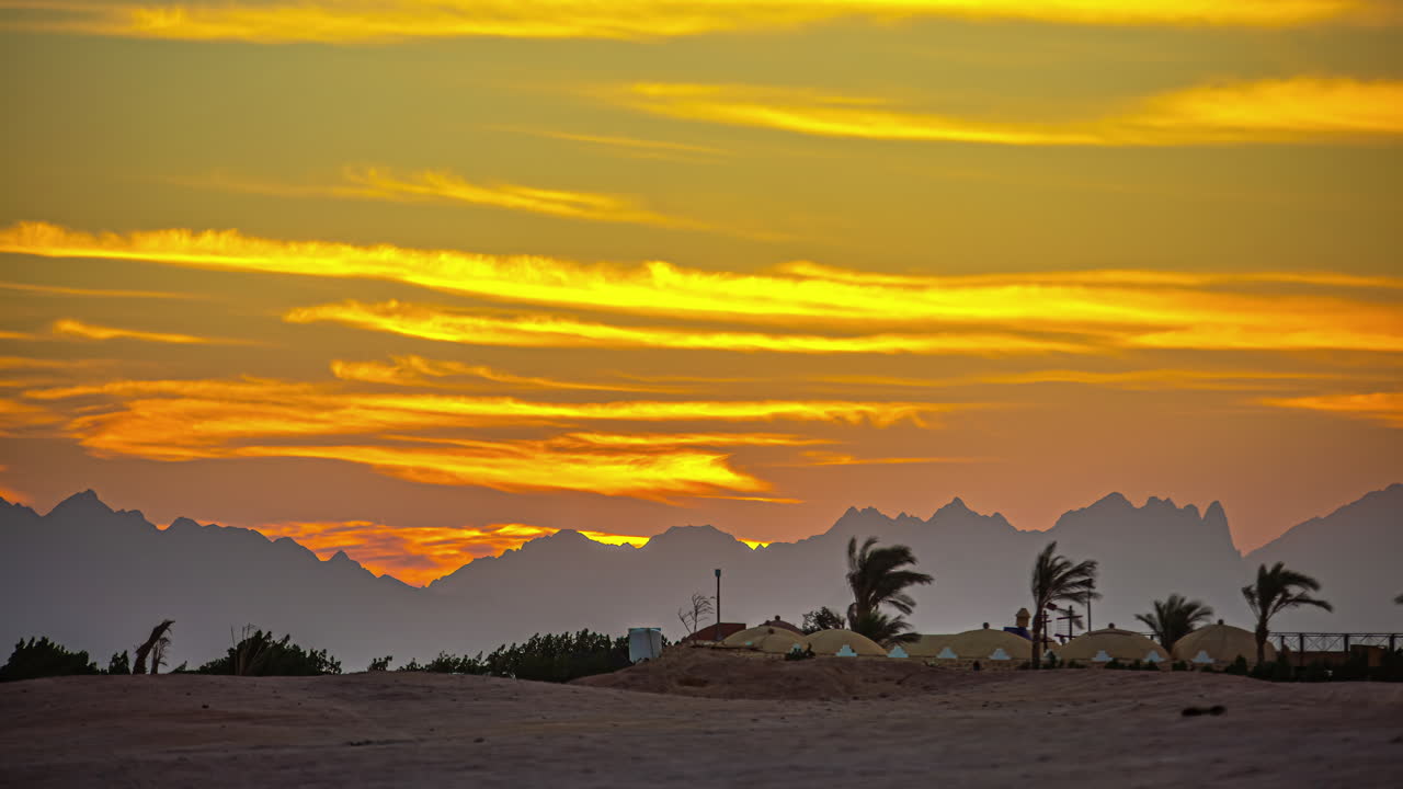 cielo naranja con nubes al atardecer sobre un paisaje desértico con palmeras y montañas en el horizonte
