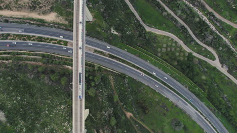 Passenger-train-crossing-on-a-Huge-bridge-and-vehicles-driving-below-it-at-the-entrance-to-Jerusalem,-Israel---over-the-Kidron-Valley---the-train-arrives-from-Tel-Aviv---Top-down-Static-shot