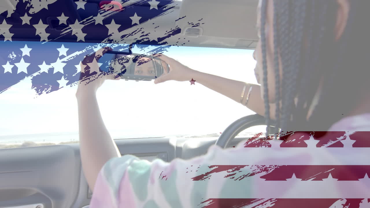 Animation of flag of usa over african american woman in car by beach in summer
