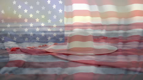 Animation-of-american-flag-blowing-over-beach-towel-and-sunhat-on-sunny-beach