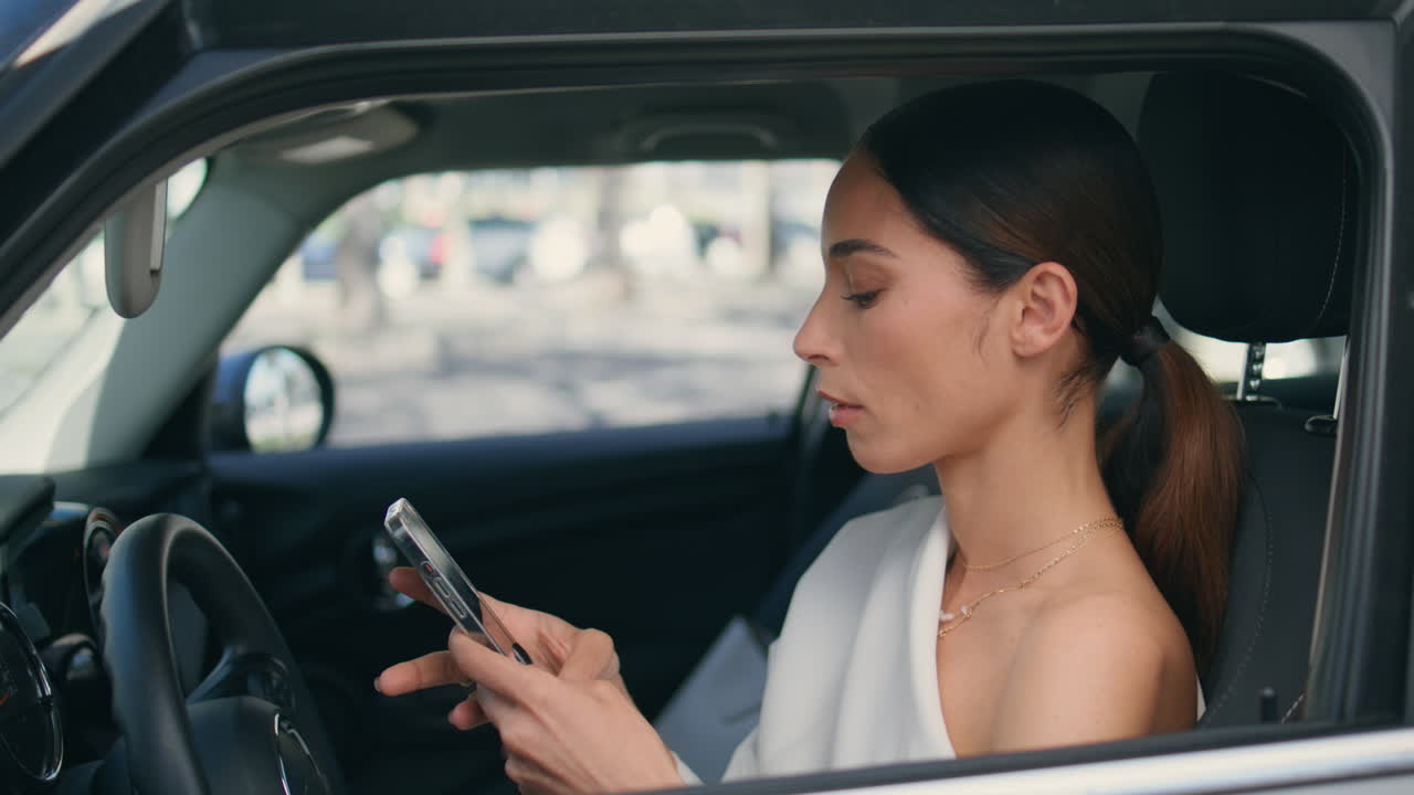 teléfono inteligente conductor sentado en la rueda del coche mirando la ventana de cerca. mujer elegante desplazamiento