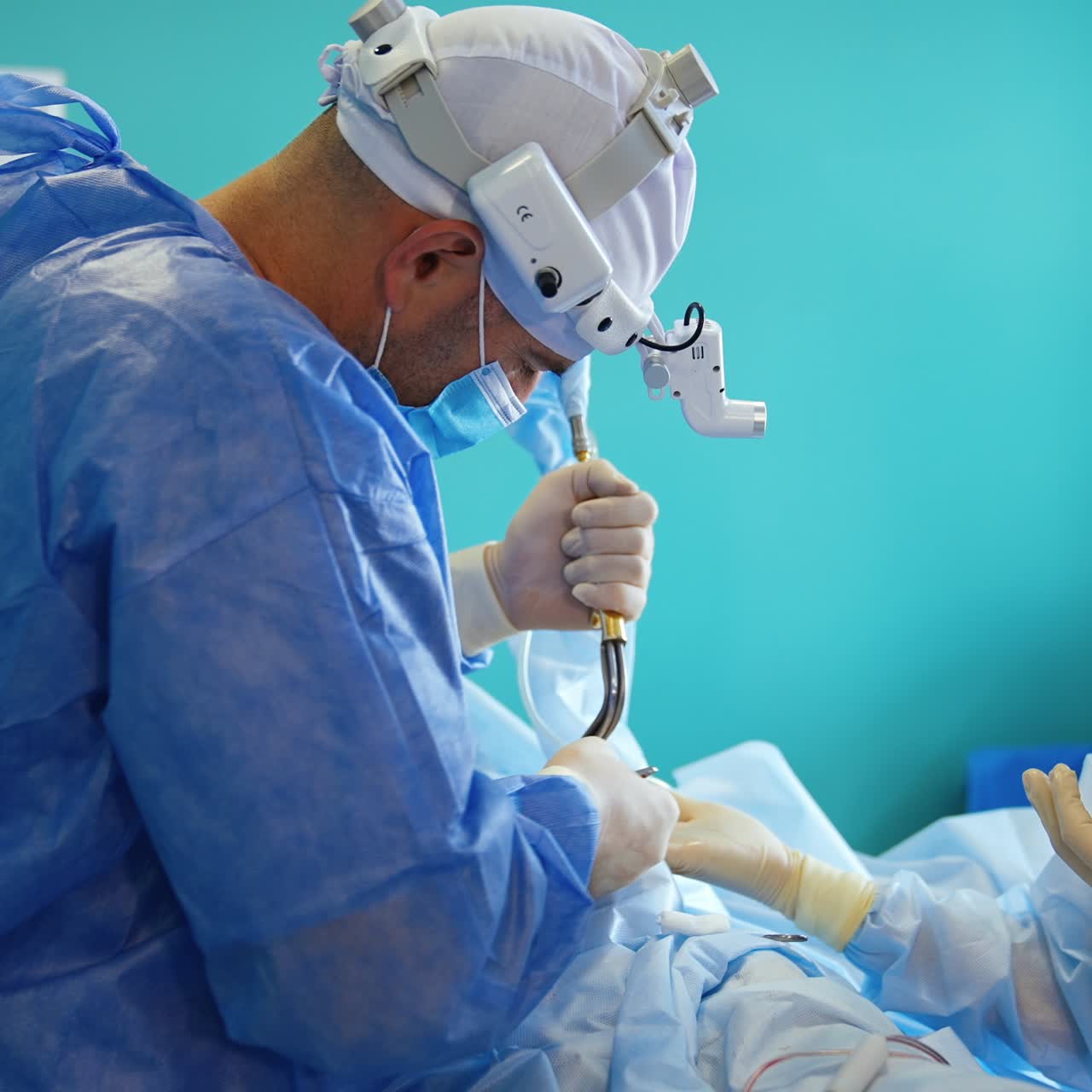 Female nurse giving a tissue to the operating surgeon. Surgeon holding instruments in both hands performing operation