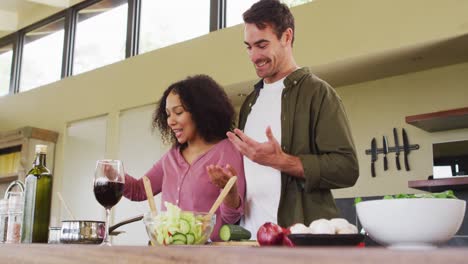 Glückliches,-Vielfältiges-Paar,-Das-Gemeinsam-In-Der-Küche-Eine-Mahlzeit-Zubereitet,-Essen-Umrührt-Und-Lacht