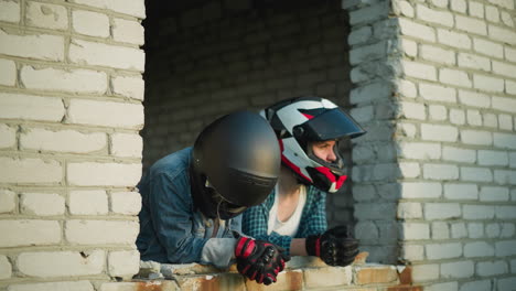 two women in helmets resting on the ledge of an old building window, one looks thoughtfully into the distance while the other gazes downward