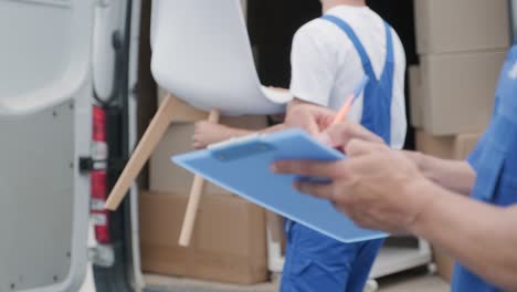 dos jóvenes trabajadores de una compañía de mudanzas están cargando cajas y muebles en un minibus