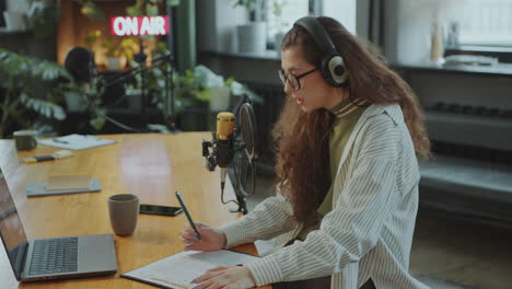 joven periodista usando portátil y planificador durante la grabación de podcast