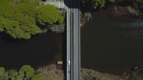 modern cars driving over a river bridge from above along a countryside street filmed and followed in bird view by aerial drone