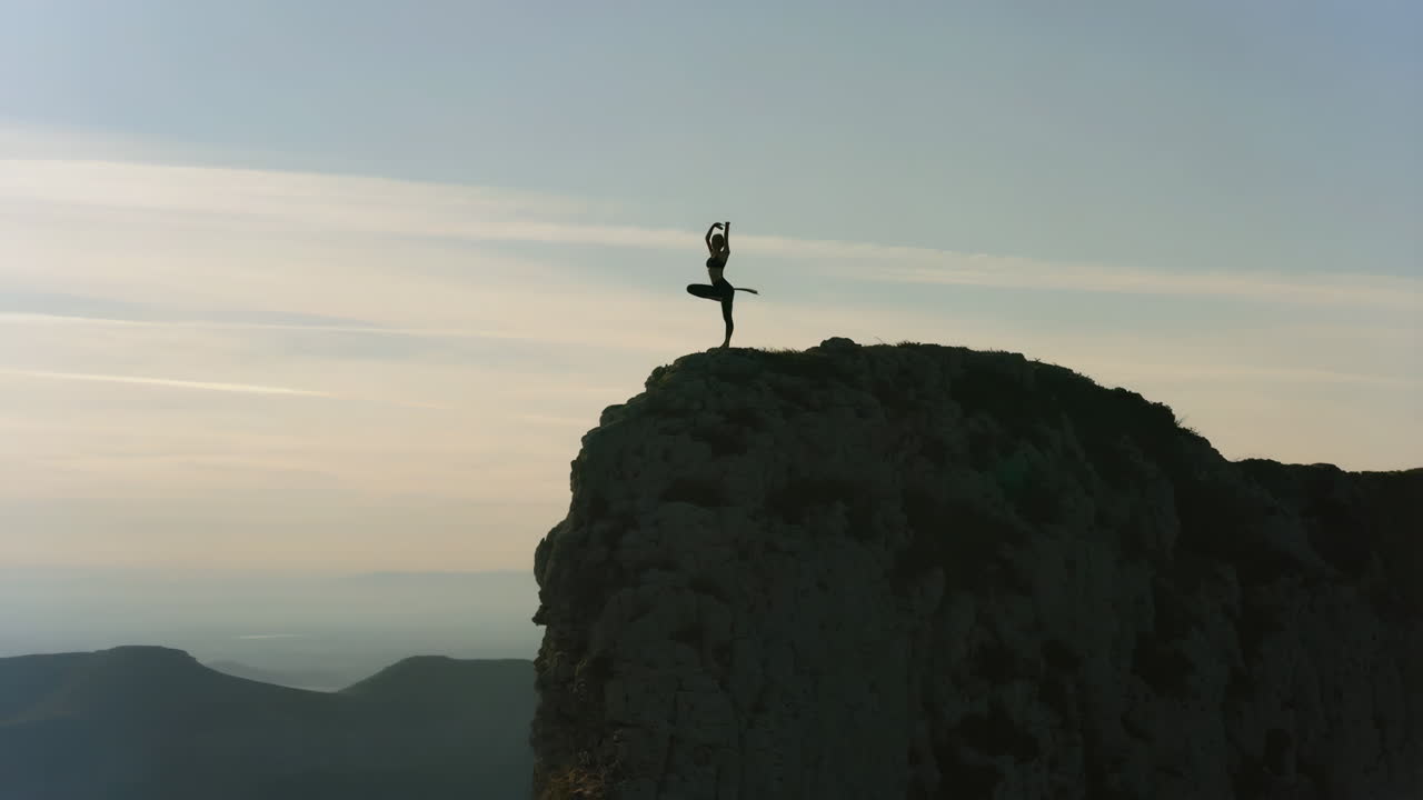 Silhouette of a person performing yoga on a mountain peak