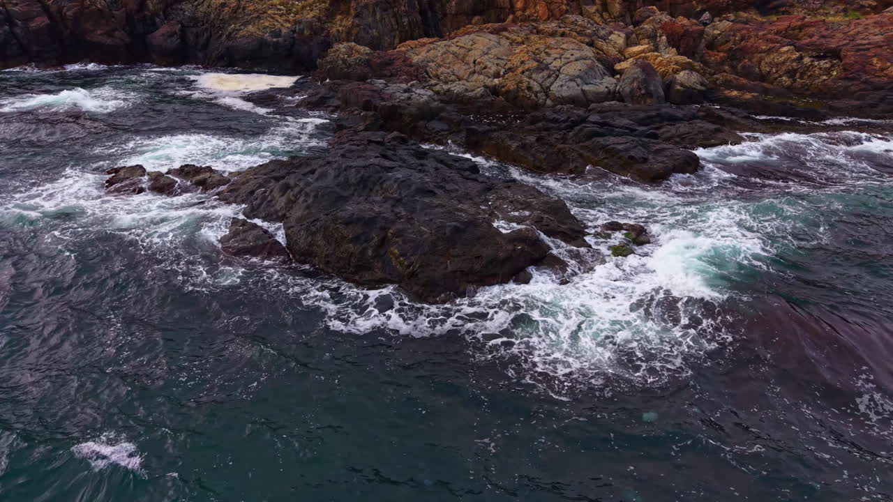 Le onde si infrangono sulle rocce frastagliate mentre il sole tramonta su un sereno paesaggio costiero, ricco di movimento e tranquillità.