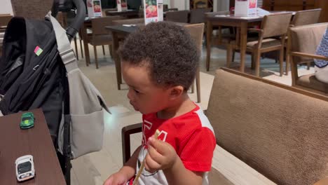 cute two year old black kid eats italian grissini for the first time, seated inside a restaurant