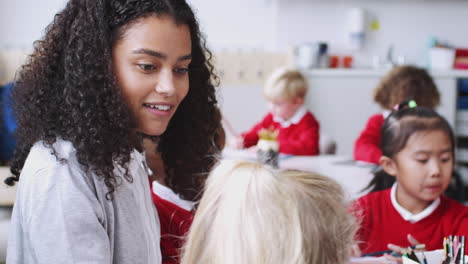 close up of millennial female infant school teacher sitting with kids in a drawing class, side view