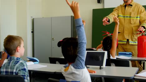 Schulkinder-Heben-Die-Hände,-Während-Ein-Männlicher-Feuerwehrmann-Im-Klassenzimmer-über-Brandschutz-Unterrichtet-4k