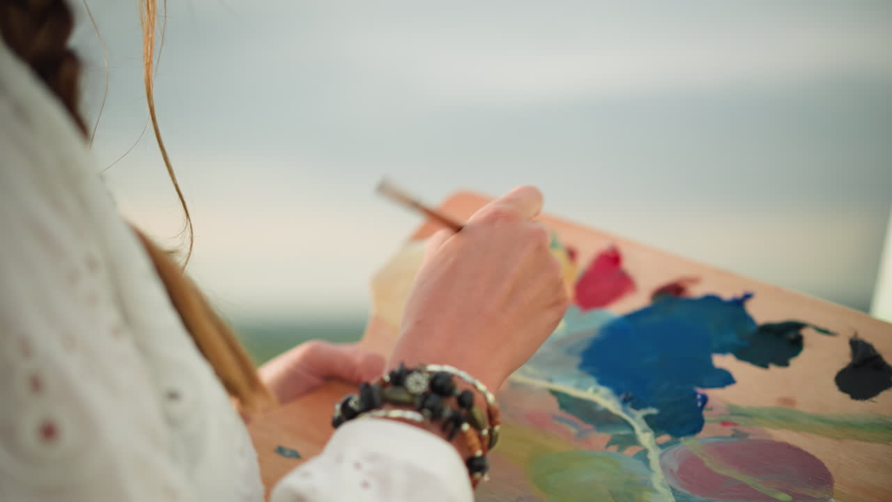 으로 장식된 여성의 손의 클로즈업, 으로 색을 부드럽게 는, 이 장면은 부드러운 빛 아래 페인트를 는 섬세한 움직임을 포착합니다.