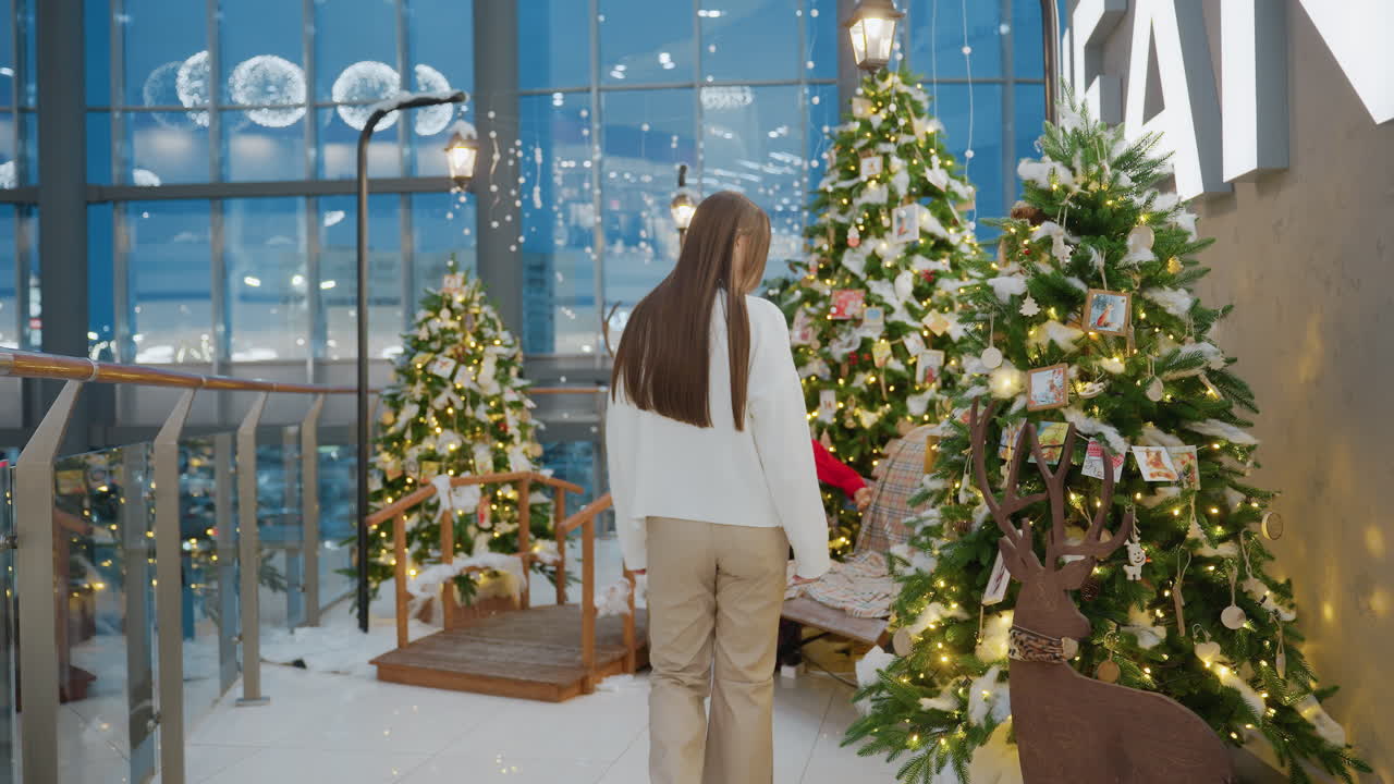 Lady walking up to decorative seats in a Christmas-themed mall area with beautifully decorated trees and lights, Santa figure, and snow setting