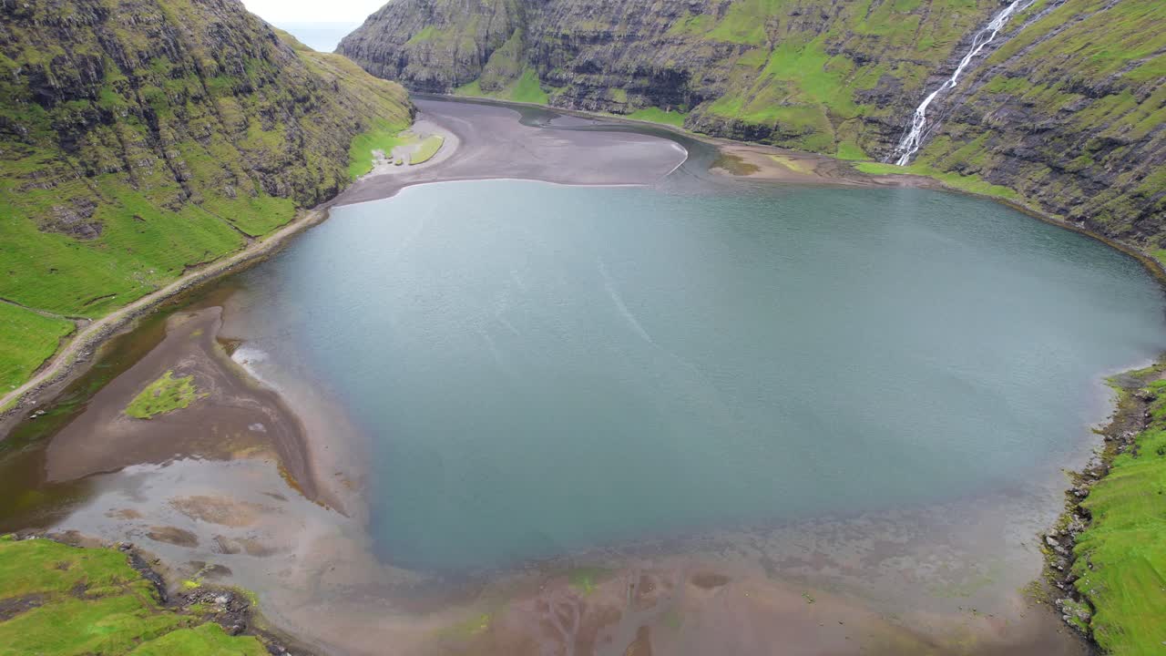 Drone flying over Saksun's lagoon surrounded by mountains in Faroe Islands