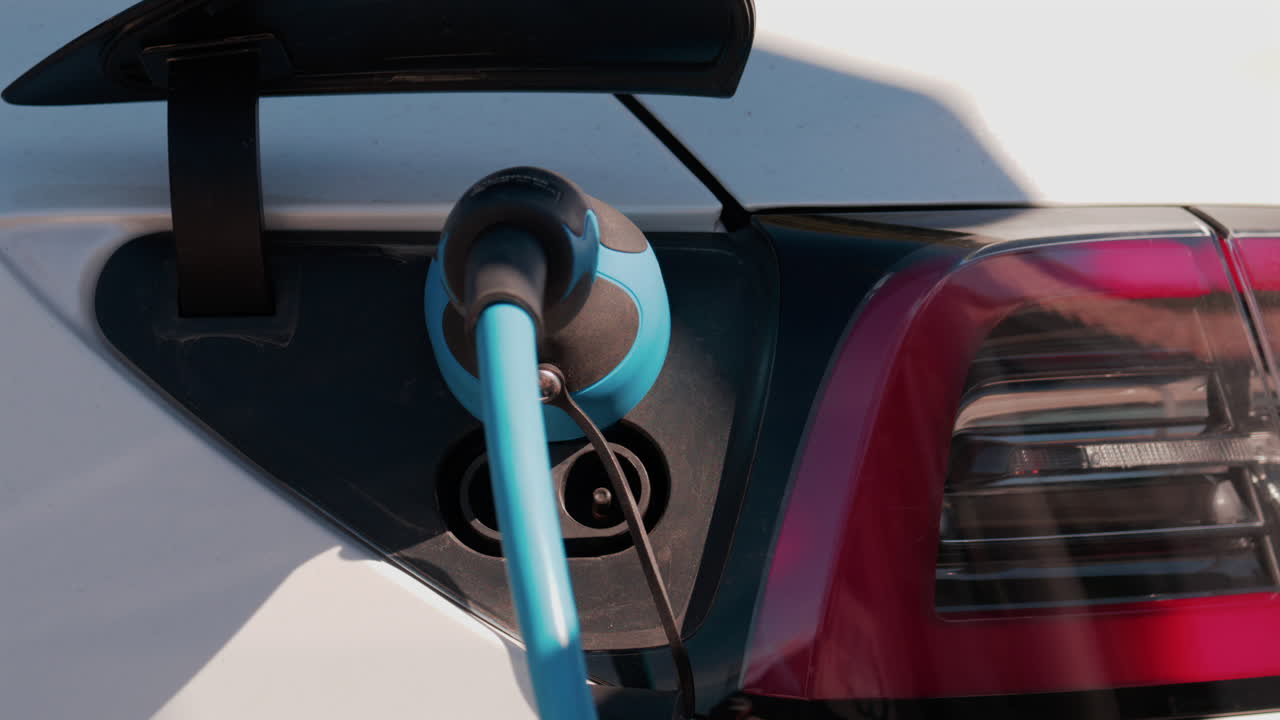 Close up of an electric car plugged into a blue charging cable in daylight