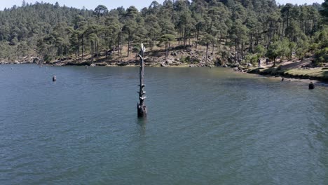 Aerial-Orbit-Circling-Vertical-Tree-Trunk-Floating-Upright-in-Blue-Forest-Lake