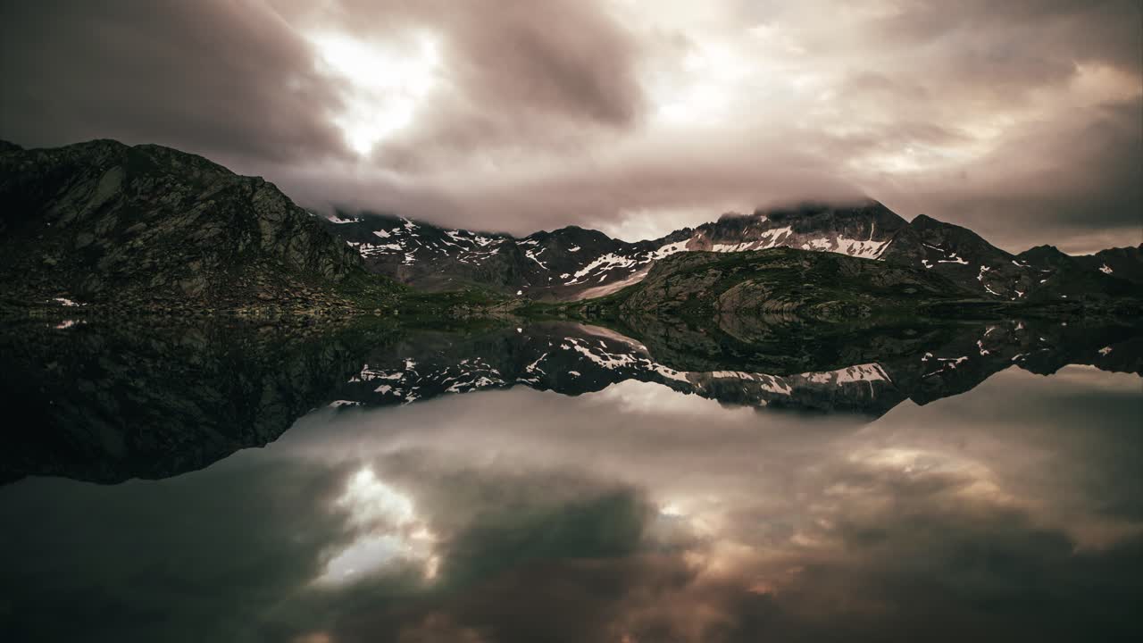 Time-lapse in the mountains with reflections in a lake and moving clouds