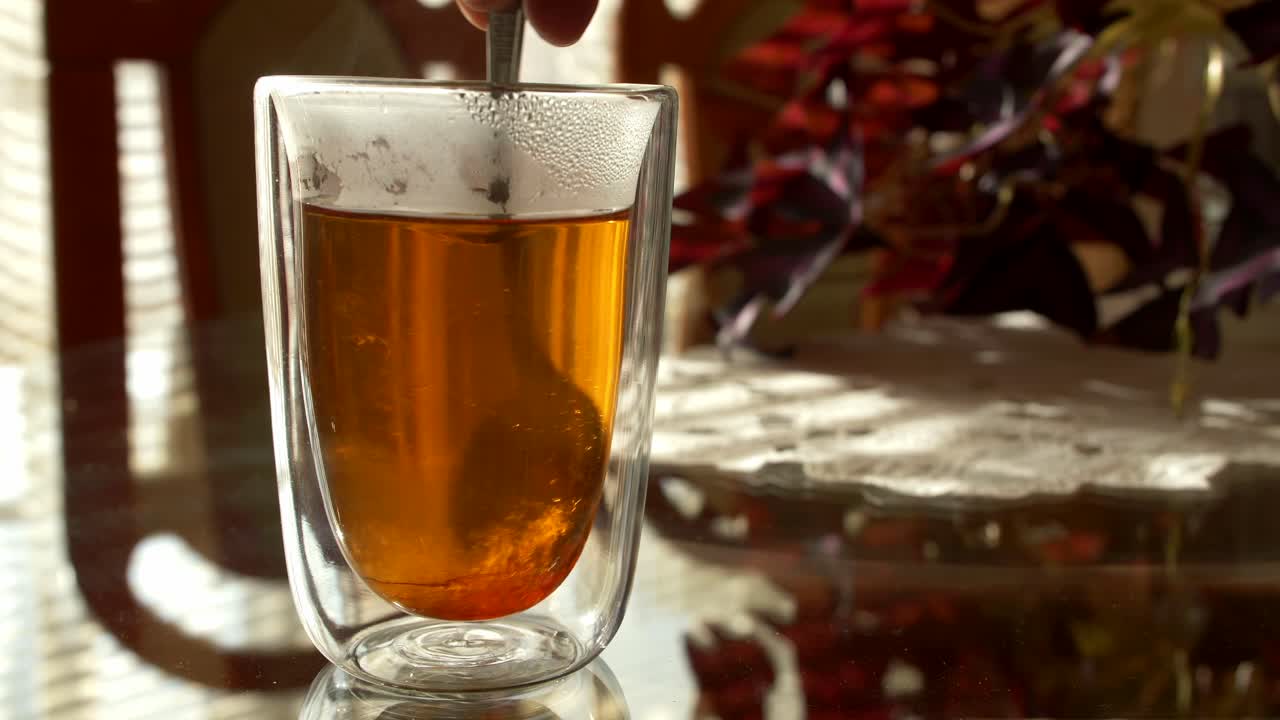 Stirring honey in a transparent glass of tea. Slow motion.