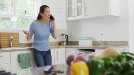행복 한 아시아 여자 는 주방 에서 스마트폰 을 사용 하고 카운터탑 에 서 있다