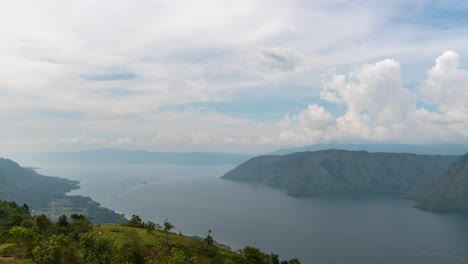 panoramic view of a vast lake surrounded by lush mountains and cloudy sky