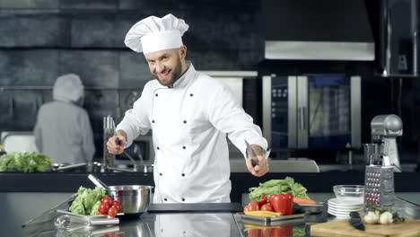 Chef-man-making-fun-at-kitchen-restaurant.-Smiley-male-chef-posing-with-knives.