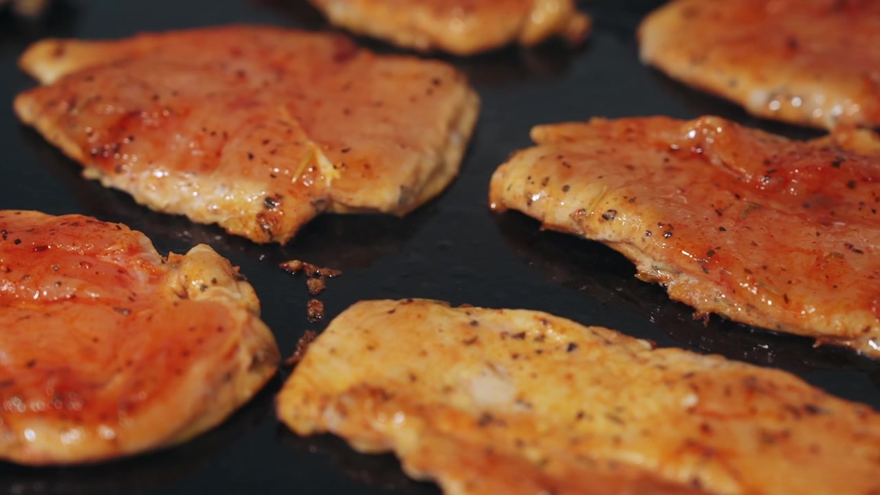 Carrellata ravvicinata che scorre su filetti di pollo conditi che cuociono e si dorano su una piastra commerciale calda
