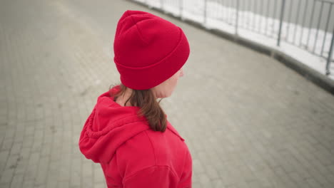 woman in red hoodie lifting head backward and forward slowly in snowy outdoor scene with iron railing in background, evoking peaceful movement and serenity in cold winter atmosphere