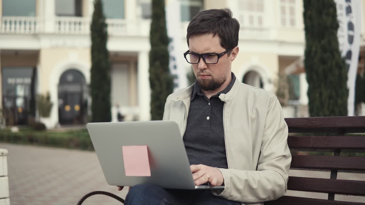 Man working on a laptop outdoors on a park bench