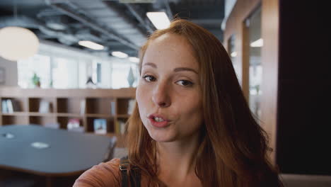 Smiling-Casually-Dressed-Businesswoman-Talks-Directly-To-Camera-Walking-Through-Open-Plan-Office