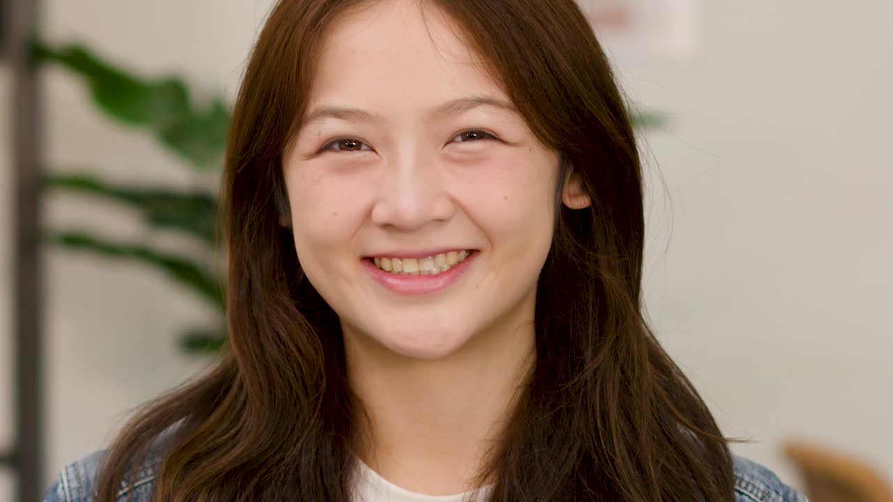 หญิงสาววัยรุ่นที่ร่าเริงยิ้มให้อย่างอบอุ่นกับกล้องในฉากในร่มที่สว่างสดใส