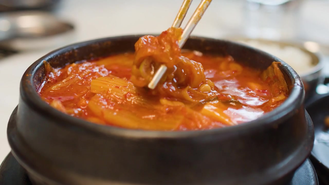 돌솥 냄비 안에서 뜨겁게 끓어오르는 김치찌개를 숟가락으로 젓는 클로즈업 샷.