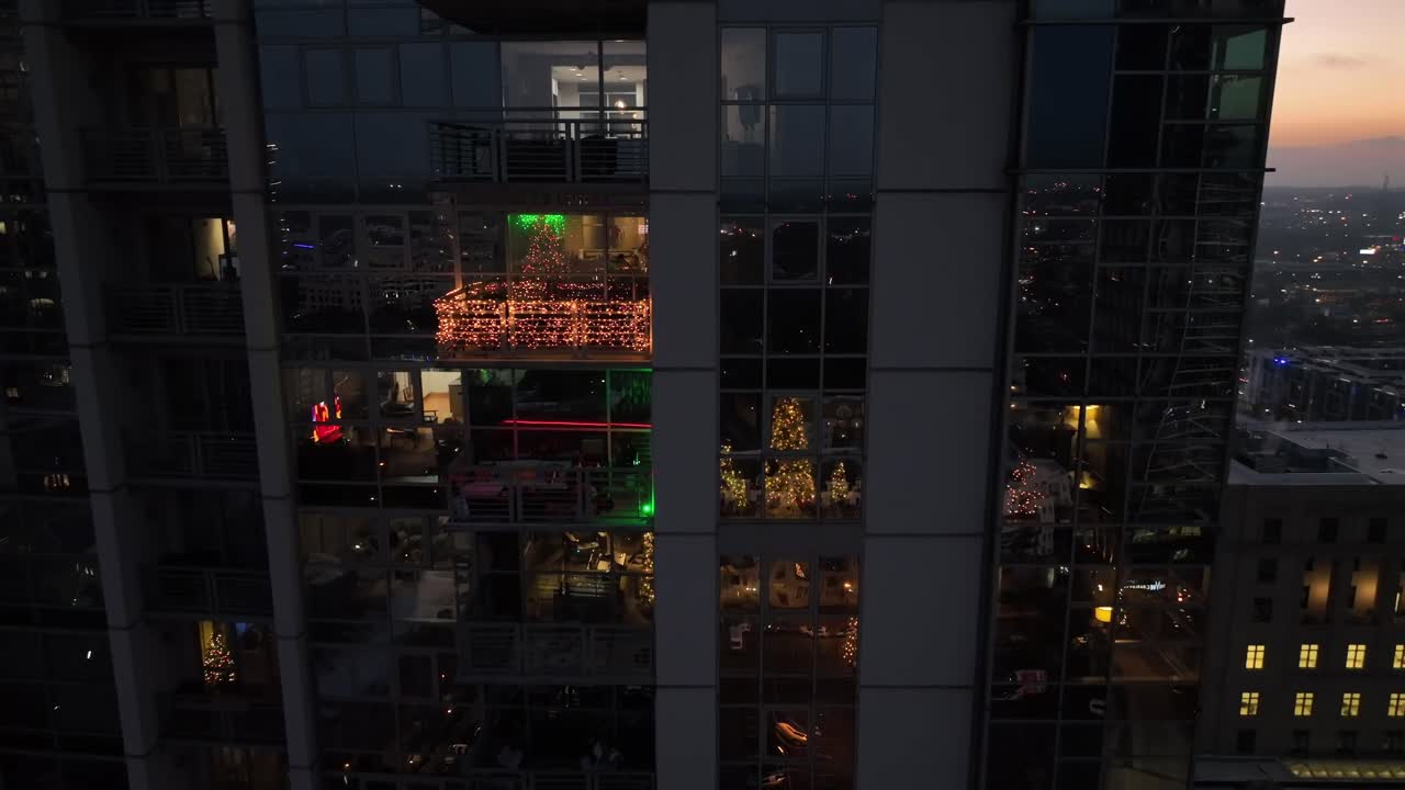 Vista aérea de um arranha-céu moderno em Charlotte ao pôr do sol, com janelas iluminadas de apartamentos refletindo as luzes da cidade dentro de um edifício de vários andares. Decoração festiva de Natal nos EUA. Plano de afastamento