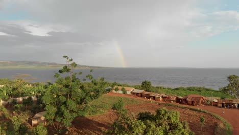 aerial shot flying over a poor village in africa with a rainbow over lake victoria in the background