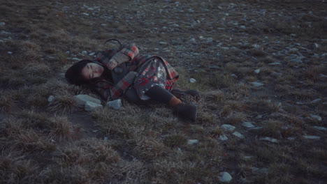 young woman lying in field at dusk, holding lantern glowing with warm light