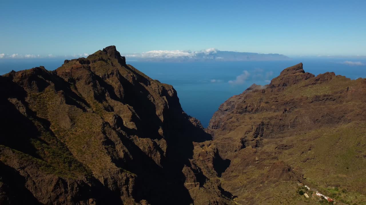 Impresionante vista de un pequeño pueblo entre montañas con el océano de fondo en Tenerife, España. Toma de dron en 4K de la isla.