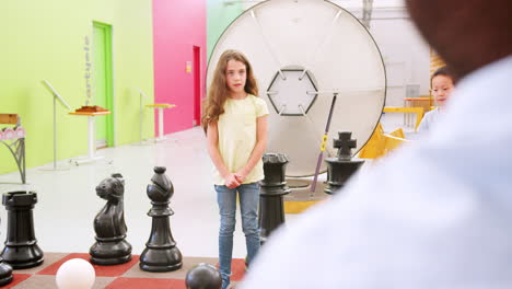 three kids playing giant chess at science centre, back view