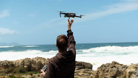 man catches and lands drone with bare hands, ocean in background