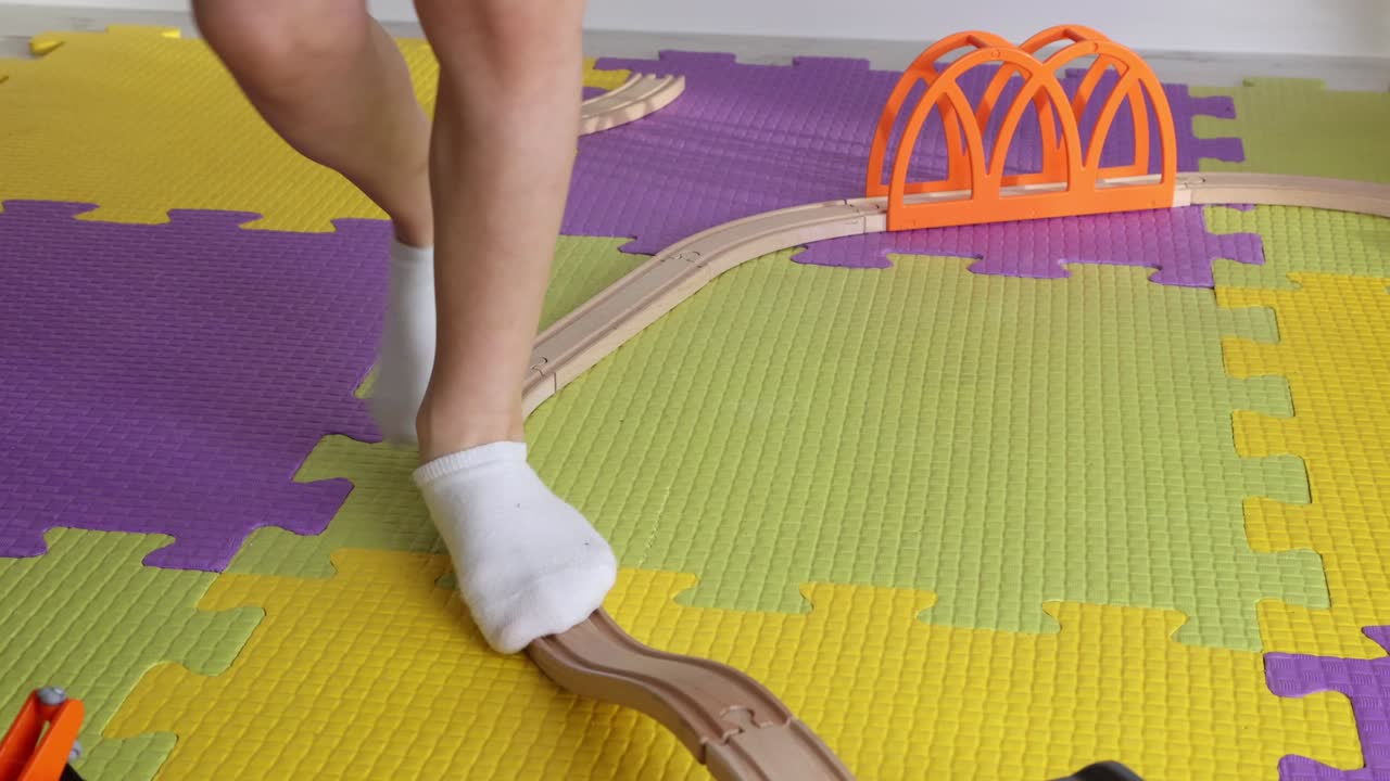 양말을 입은 아이가 장난감 나무 철도를 따라 균형을 잡고 고 있습니다.